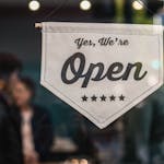 Welcoming open sign displayed in a shop window with blurred background.